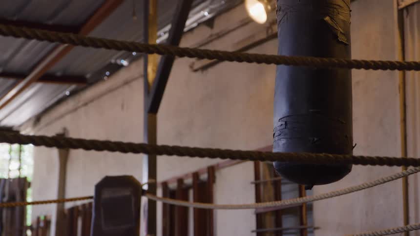 A black punching bag hanging in an indoor boxing ring during daytime