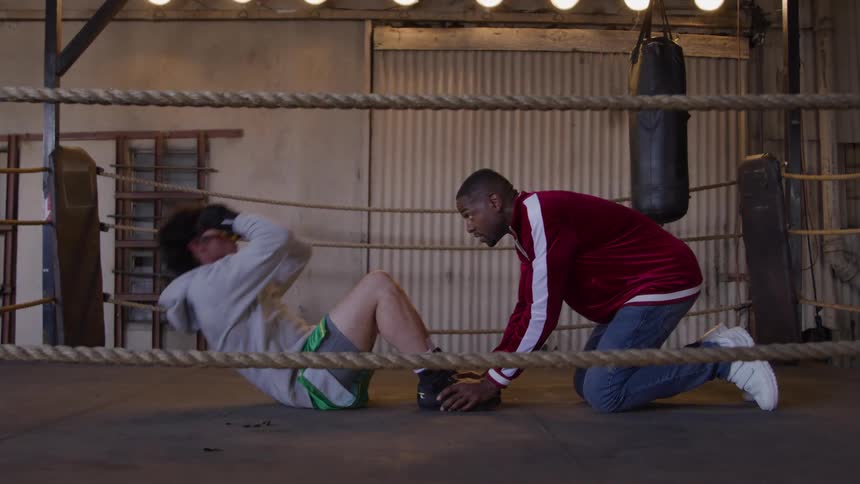 Coach motivates the boxer during a set of situps in the ring