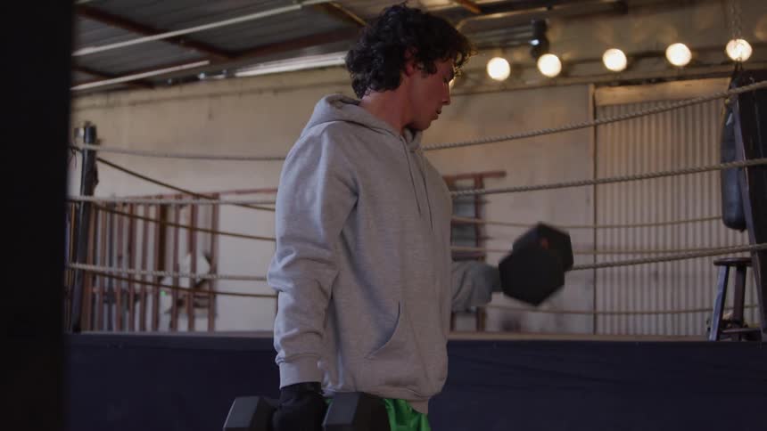 A man is a grey hoodie lifts heavy weightswith his hands in a gym