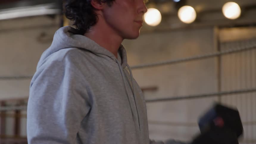 Close up of a young man lighting weights for training in an indoor boxing ring during daytime