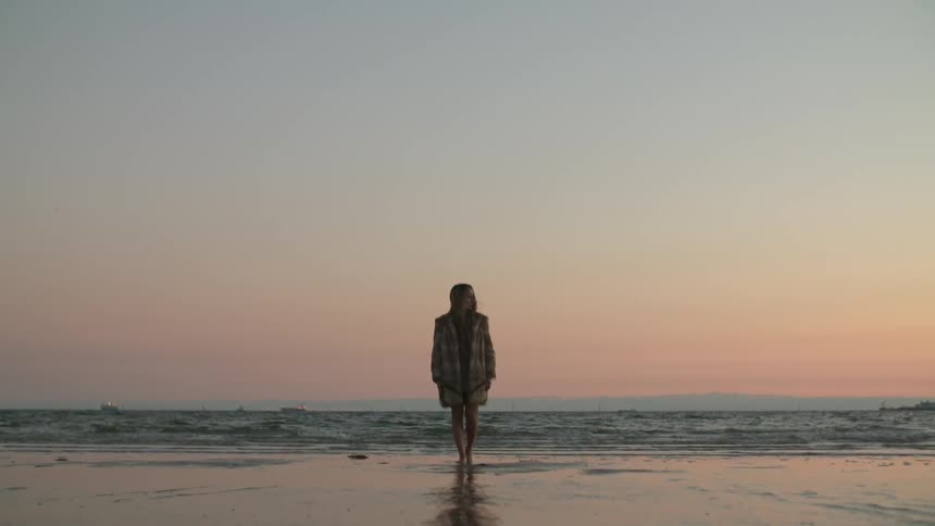 A woman stands on the beach at sunset