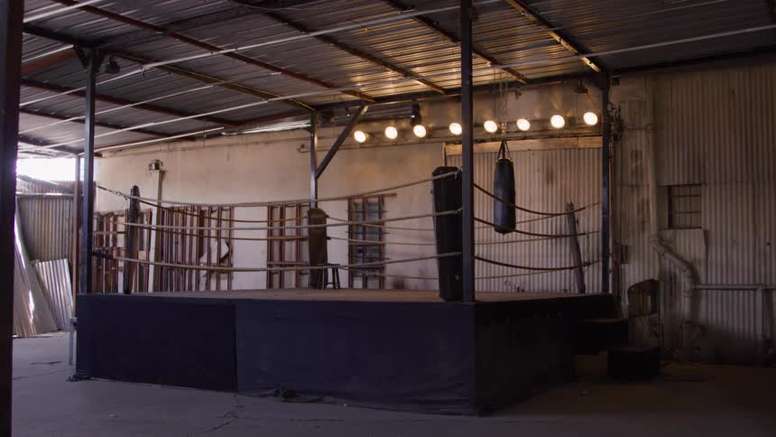 Empty boxing ring lit by yellow lights inside an industrial warehouse