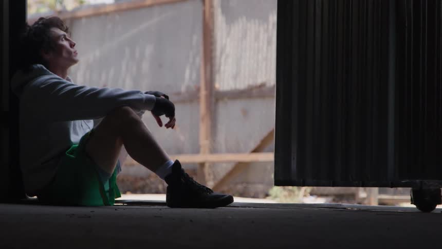 A young man sitting on the floor in a room after a sparring session during daytime