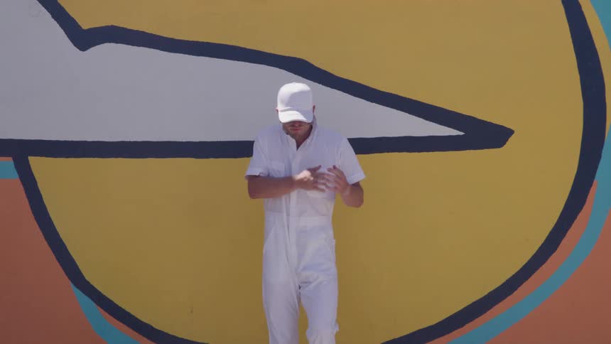 Man dressed in white dances in front of a colorful mural with geometric shapes