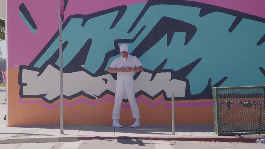 A young man dancing in front of a graffiti wall outdoors during daytime