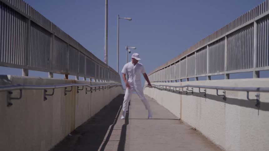 A young male dancer dancing outdoors on a pedestrian bridge during daytime