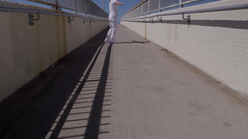 A young man dancing while walking outdoors on a pedestrian bridge during daytime