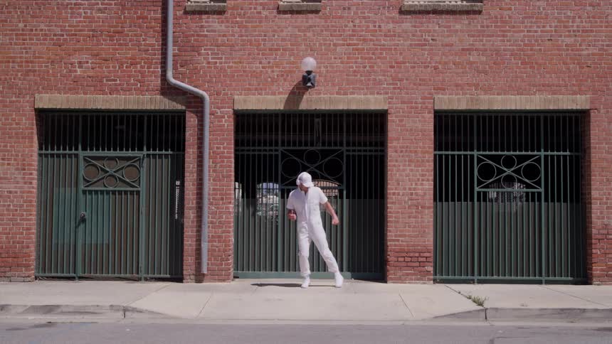Person dressed in white dancing in front of a brick wall with green metal gates