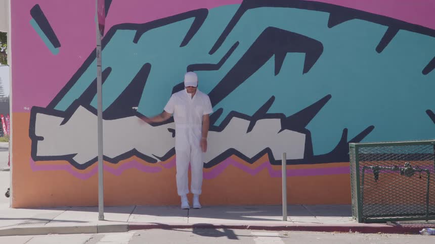 A young male dancer dancing in front of a graffiti wall outdoors during daytime