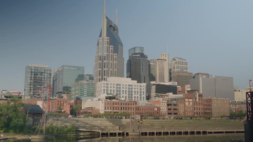 A riverfront city skyline with a twinspired tower behind rows of brick warehouses beneath a clear blue sky