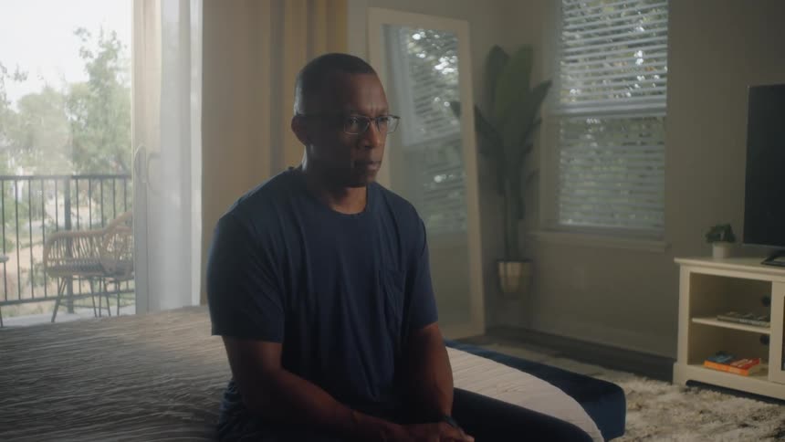 Wife comforts her upset husband in a sunlit bedroom