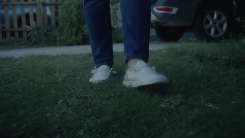 Closeup of feet in white shoes walking on grass by a parked car