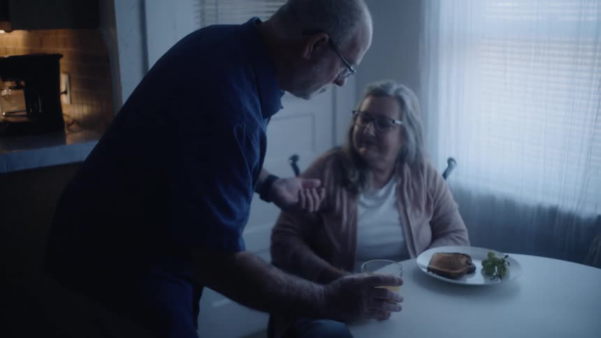 Man comforts a woman and gives her medicine at a table indoors