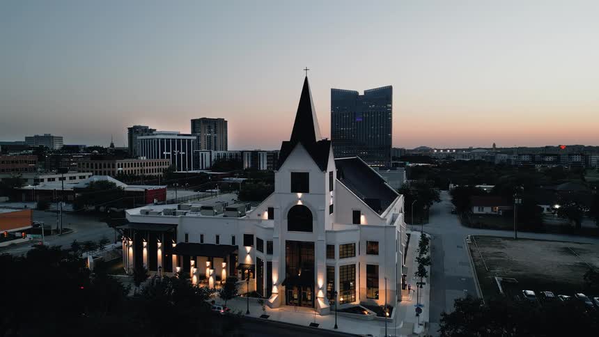 Vehicles drive past a church located near a residential area in the evening
