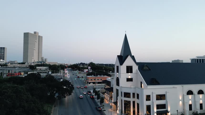 Aerial view of a city street lined with cars beside a tall white church at dusk