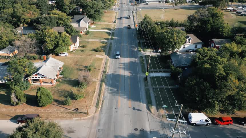 Aerial view of suburban houses with moving vehicles and trees under a bright sky