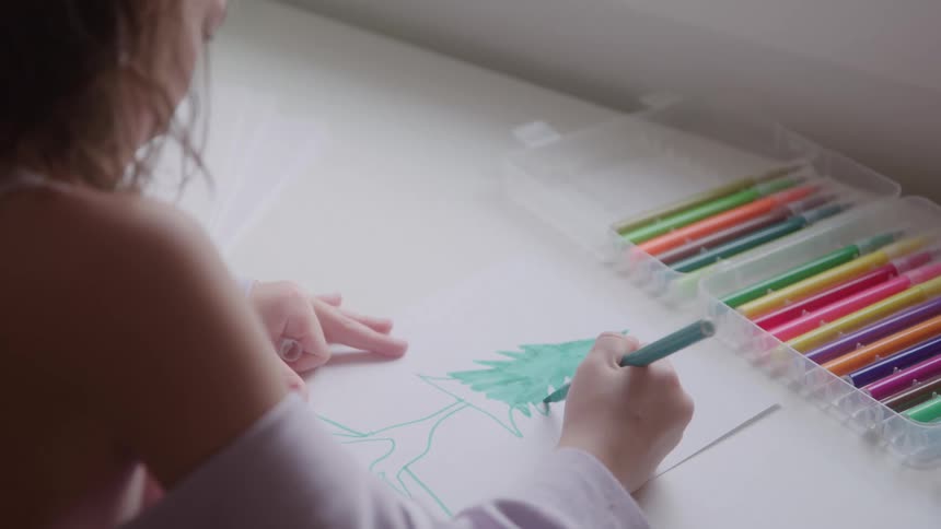 Girl fills in her drawing of a fir tree while sitting indoors