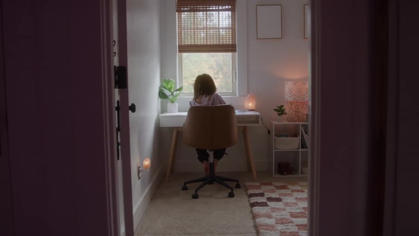 Person sitting on an office chair facing the window in a softly lit room decorated with neutral tones and plants