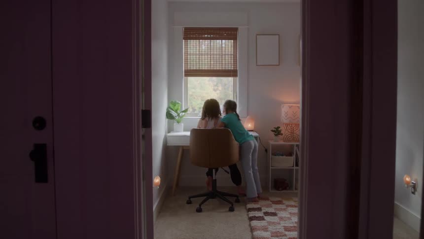 Girl runs into a room to hug an older girl sitting at a desk on an autumn day