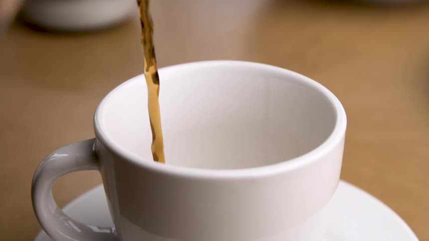Closeup of dark coffee being poured into a white cup on a table