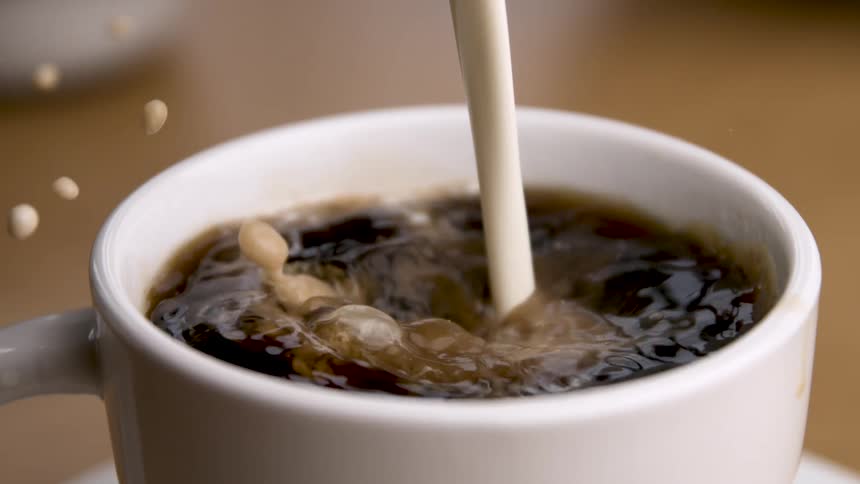 A stream of milk being poured into a white cup filled with dark liquid coffee