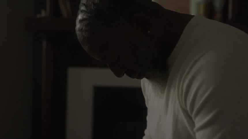 Older man bows his head and prays near the fireplace