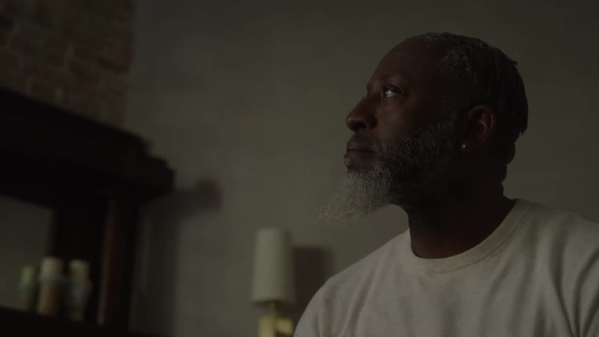 A man sits lost in deep thought in a dimly lit room