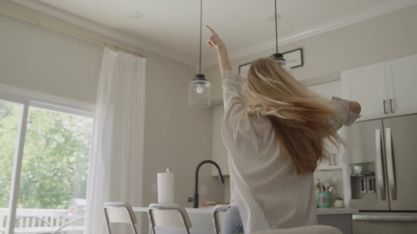 Smiling woman spinning with arms open in a bright room filled with natural light