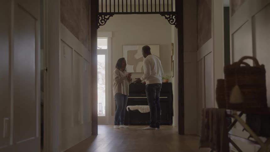 In a warmly lit hallway a man and a woman face each other midconversation with tense body language