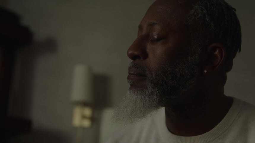 A man sits thoughtfully in a softly lit bedroom