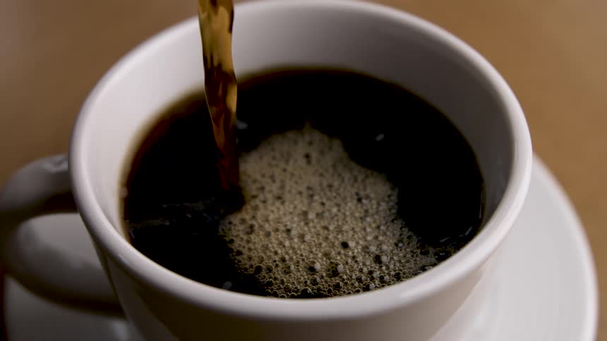 Closeup of black coffee being poured into a white cup on a table