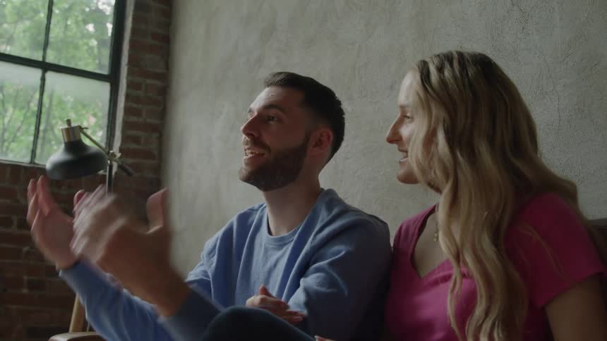 A man and woman sit together smiling and engaged as he gestures animatedly near a window