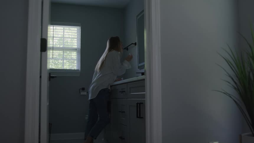 Woman doing her makeup in front of the bathroom mirror lit by natural light