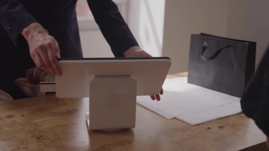 Person operating a payment terminal on a wooden table beside a black shopping bag