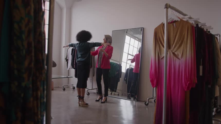 Woman taking measurements of another in a clothing store