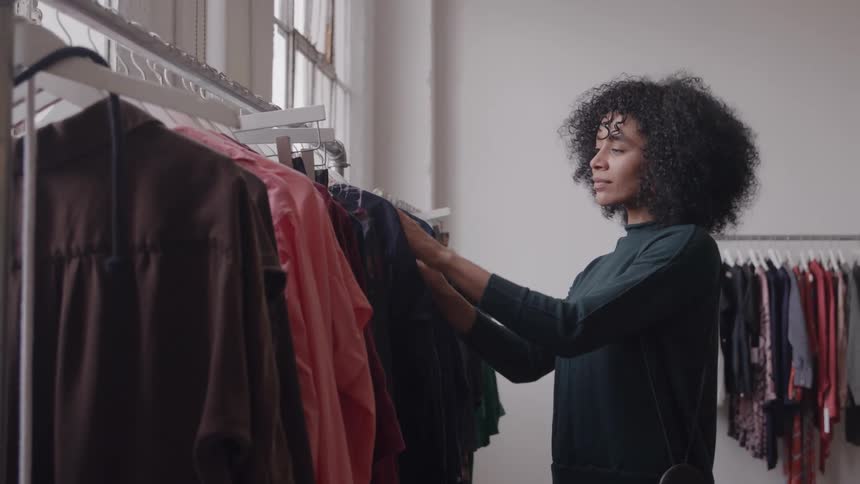 The woman is browsing through clothes as she shops