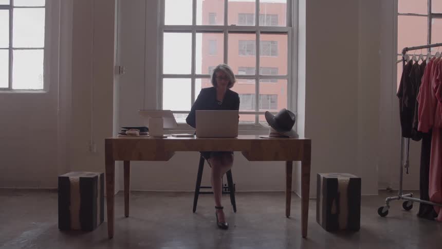 Woman working on a laptop in a fashion studio lit by large windows