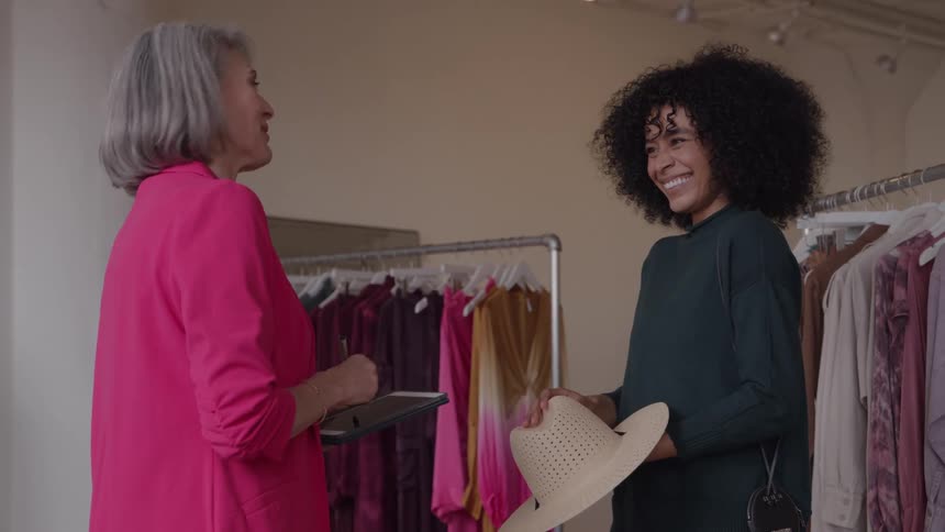 Two women laugh and interact in a fashion studio