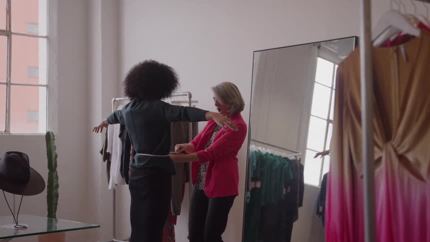 Seamstress adjusting a clients waist in a fashion studio lit by natural light