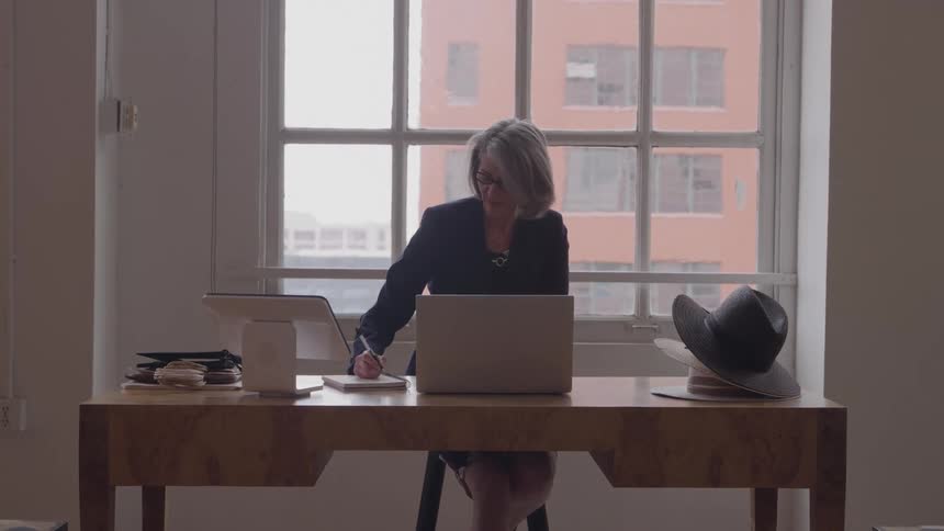 Grayhaired woman working on a laptop in an office lit by large windows