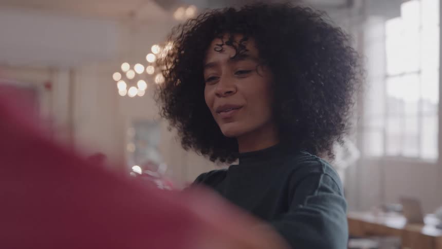 The video features a young woman with curly hair who looks directly at the camera with a cheerful wide smile the background is bright with a hint of red fabric in the foreground