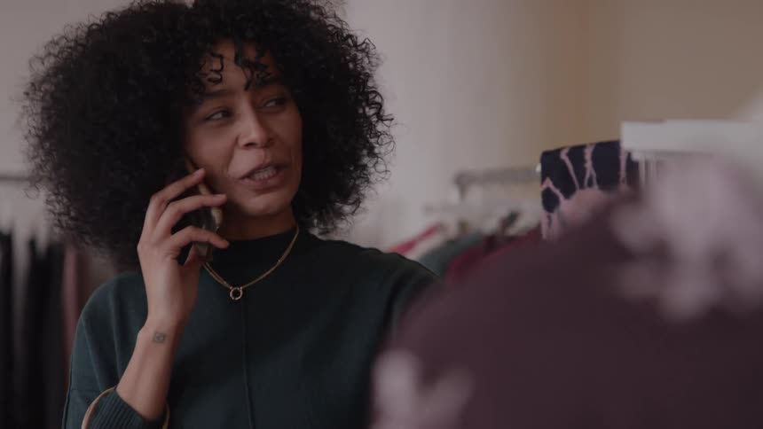 Woman talking on the phone while looking at a piece of clothing in a store
