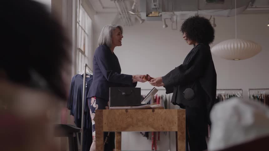 A saleswoman helps a client at a wooden counter in a bright boutique