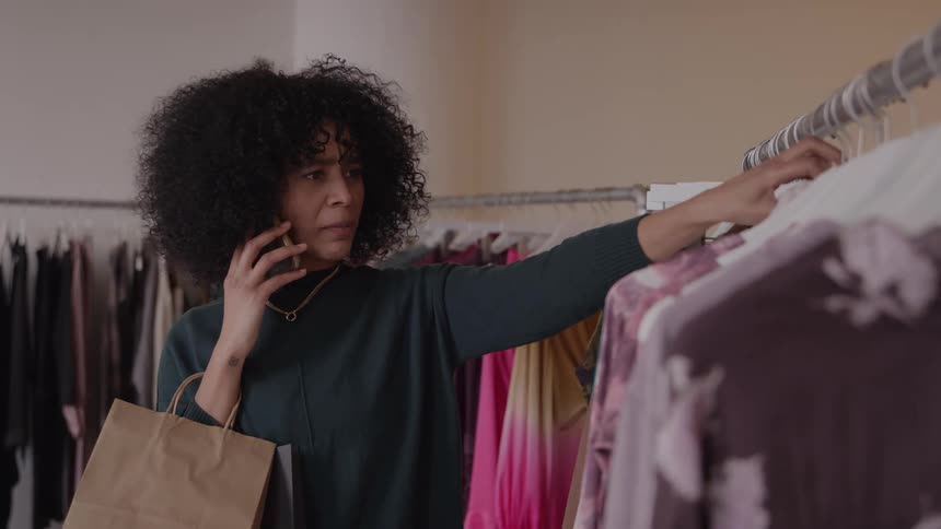 Woman talking on the phone while selecting clothes on a store rack