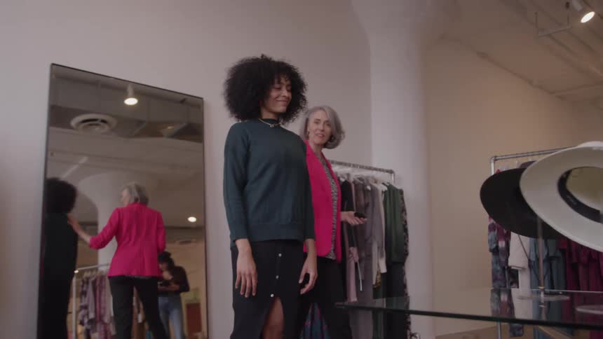 A personal stylist helps a young woman pick out an outfit in a chic clothing boutique