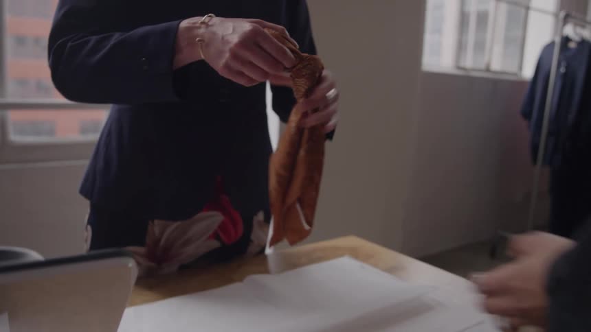The video shows a transaction taking place at a checkout counter in a clothing storeone person is handing an orange bow or scarf to the other person across a wooden counter