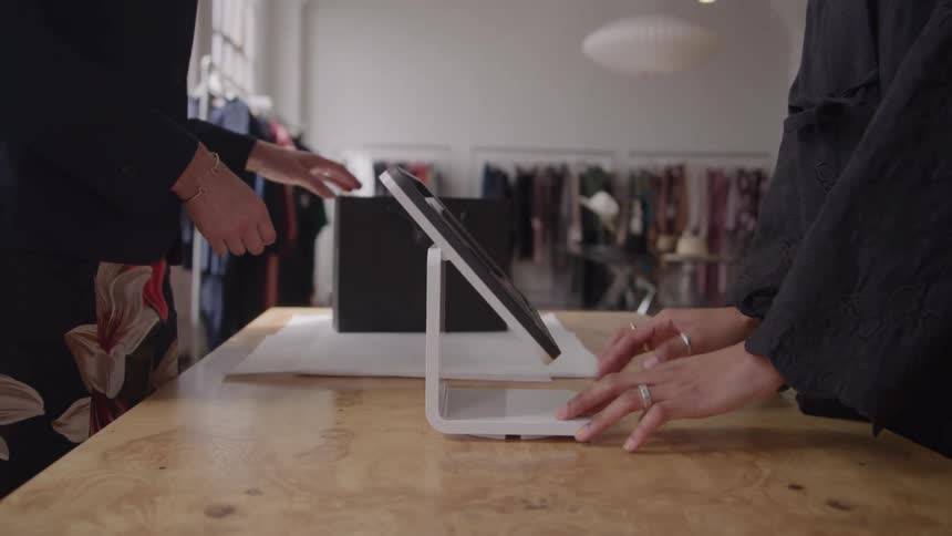 A customer uses a credit card to pay at a counter in a clothing boutique as an associate takes payment