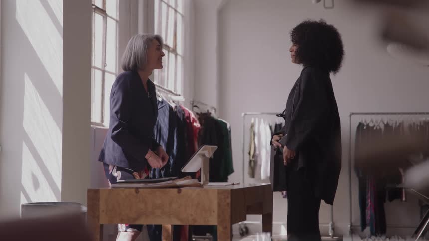 A female cashier hands a shopping bag to a customer inside a clothing shop at midday completing the transaction after processing the customers credit card payment with a friendly exchange