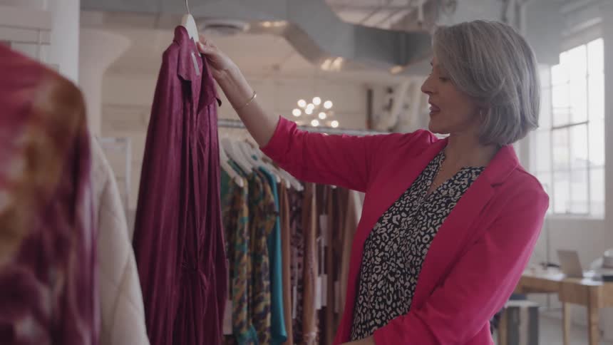 A woman is browsing a rack of dark colored clothing in a brightly lit boutique