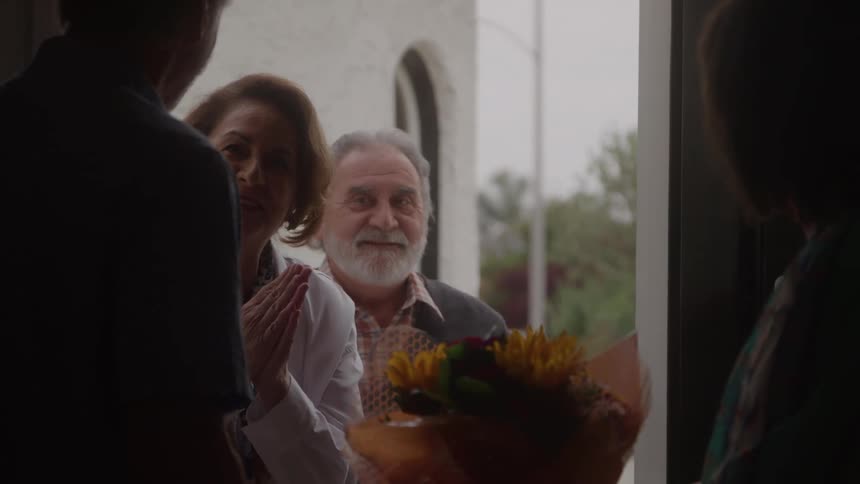 Woman at a doorway accepts a bright bouquet while speaking with visitors looking warm and appreciative